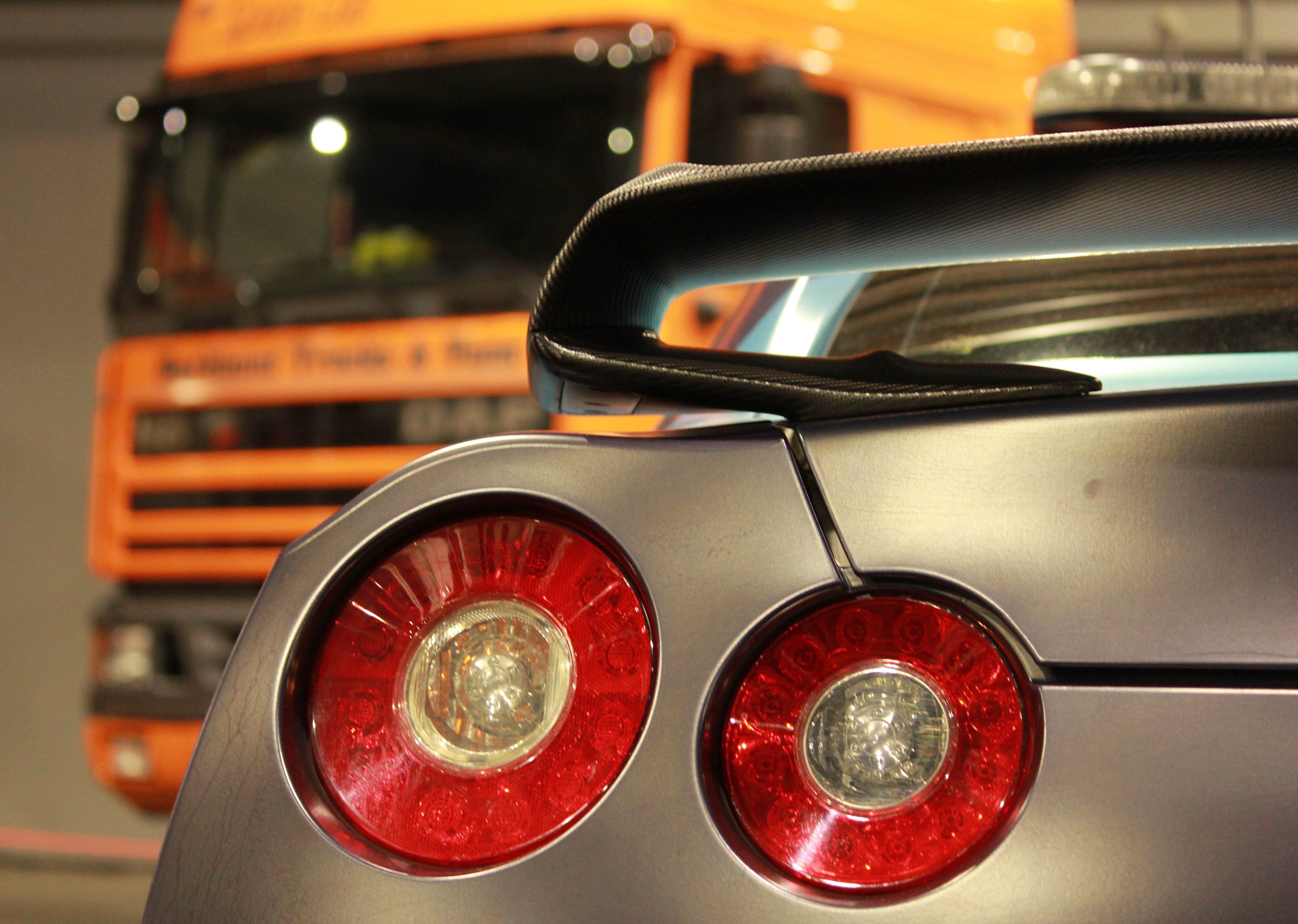 Photo of a Nissan GTR taillight with a orange truck blurred in the background